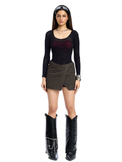 Woman wearing a black long-sleeve top, brown skirt, and black boots on a white background