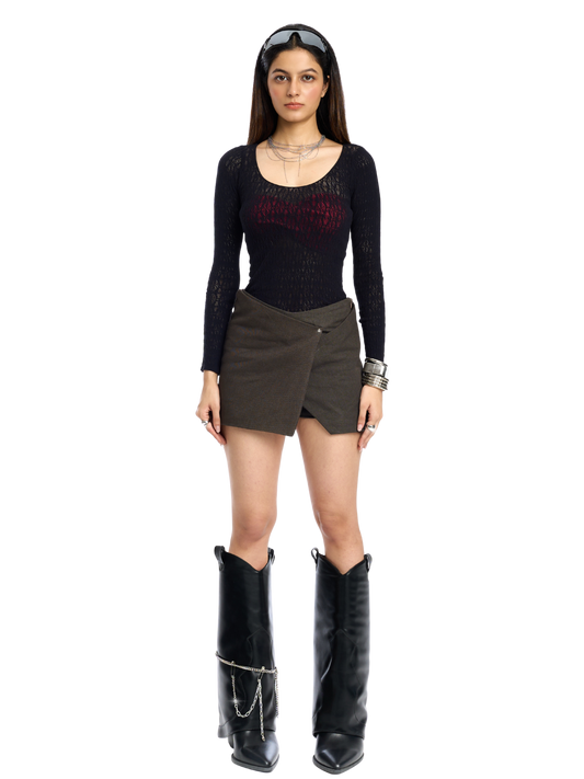 Woman wearing a black long-sleeve top, brown skirt, and black boots on a white background